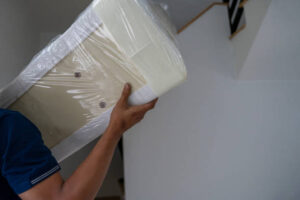A delivery person is transporting a mattress into a customer's new home