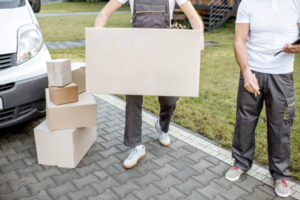 Delivery men moving cardboard boxes outdoors, delivering goods with cargo vehicle, close-up on boxes with blank space